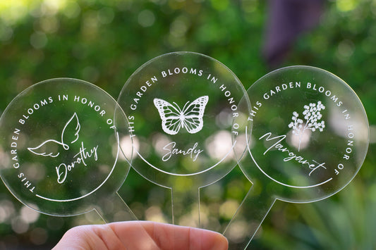 photo of three clear circular garden stakes - one that displays a flower and "Margaret" at the center and the words "This Garden Blooms In Honor Of" around the flower, one that displays a butterfly and "Sandy" at the center and the words "This Garden Blooms In Honor Of" around the butterfly and one that displays angel wings and "Dorothy" at the center and the words "This Garden Blooms In Honor Of" around the angel wings