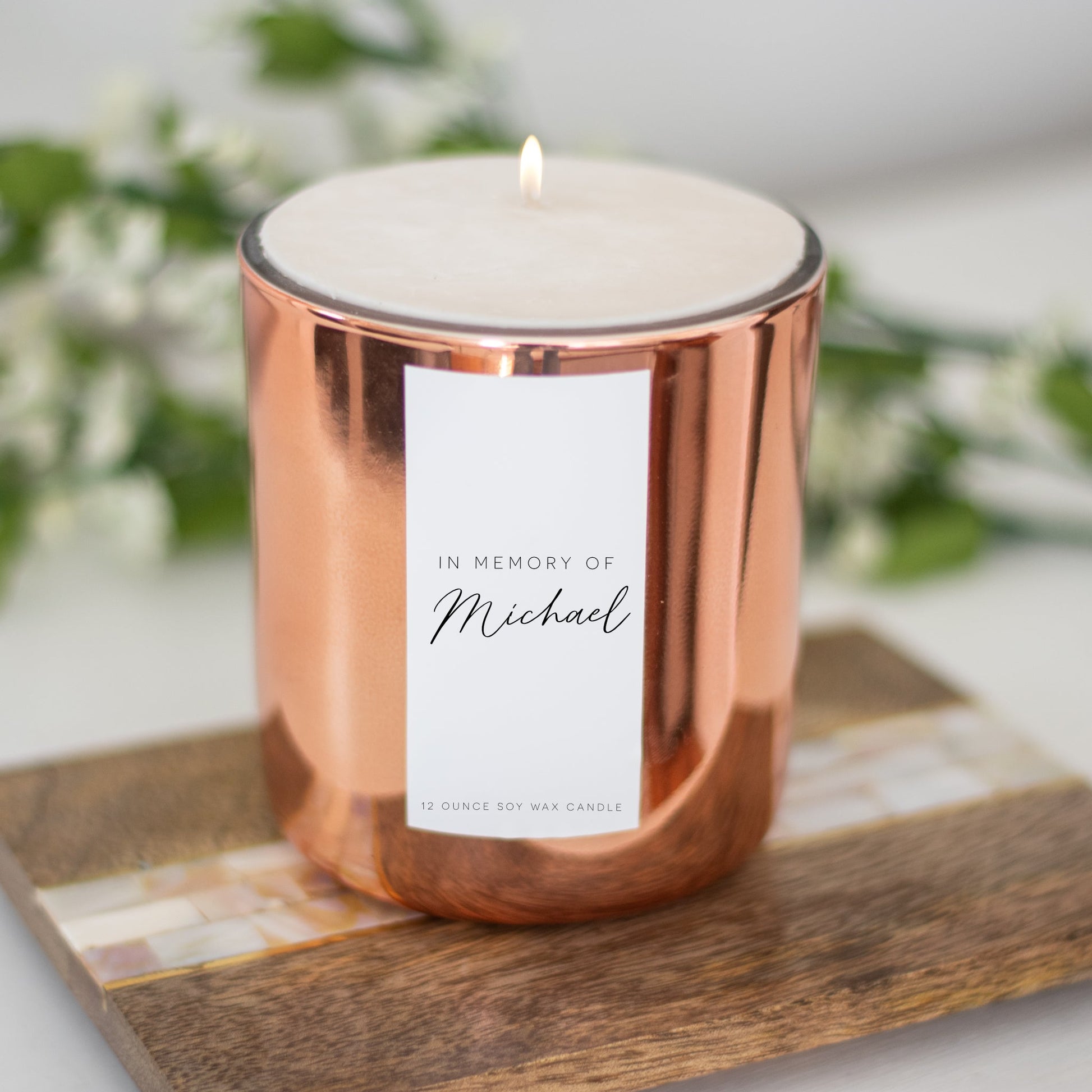 A gold-coated candle with a white sticker with the text In Memory of Michael resting on a wooden coaster