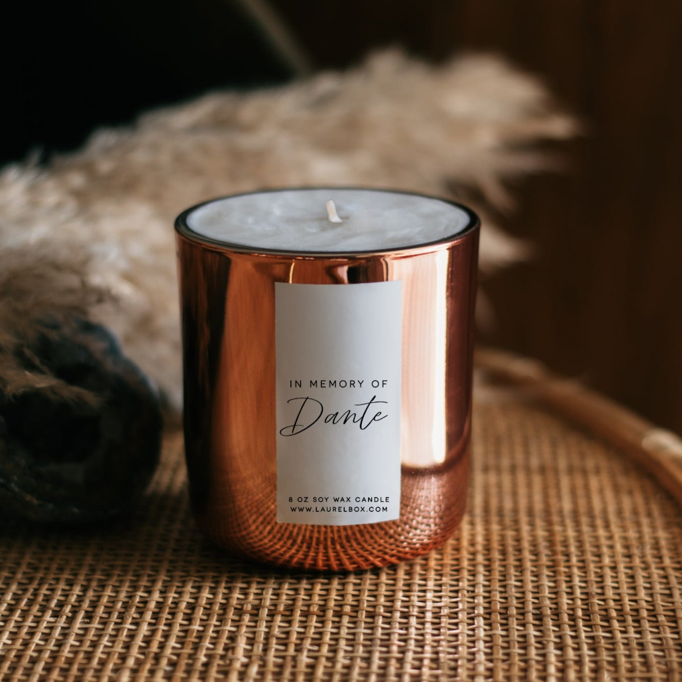 A gold-coated candle with a white sticker with the text In Memory of Dante sitting on a coffee table