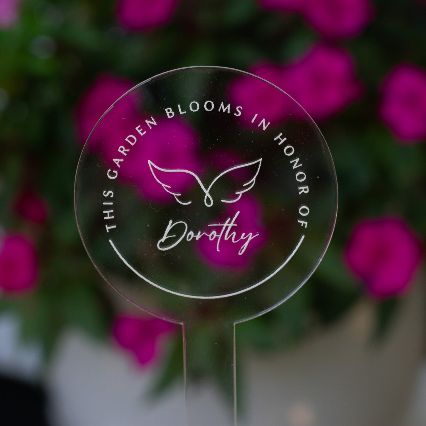 photo of a clear circular garden stake that displays angel wings and  "Dorothy" at the center and the words "This Garden Blooms In Honor Of" around the angel wings
