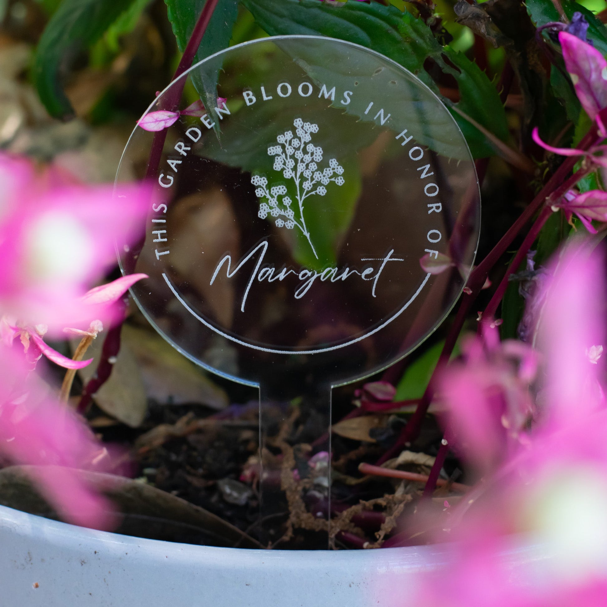 photo of a clear circular garden stake that displays a flower and  "Margaret" at the center and the words "This Garden Blooms In Honor Of" around the flower