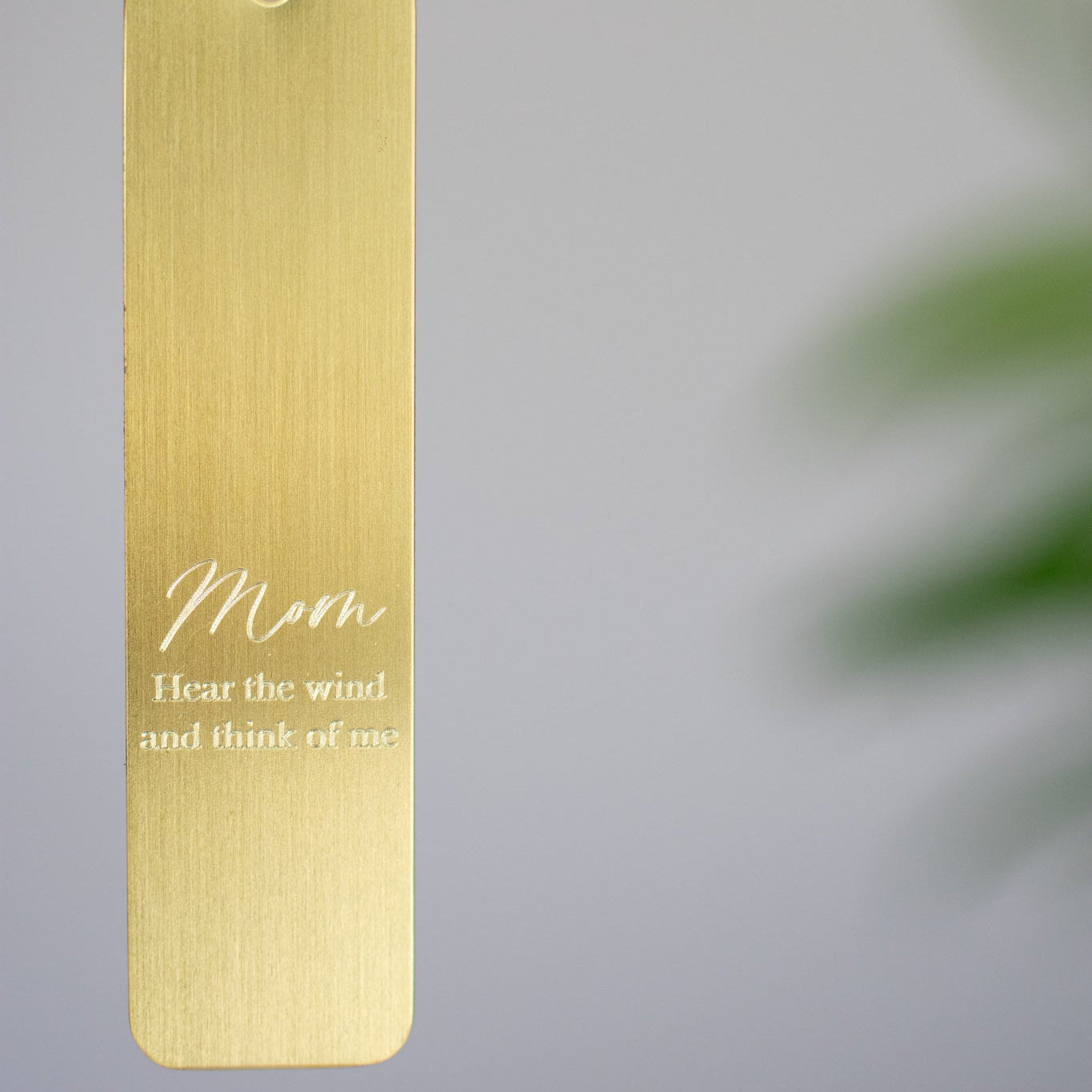 close up photo of an engraved gold rectangle with the words "Sarah hear the wind and think of me" 