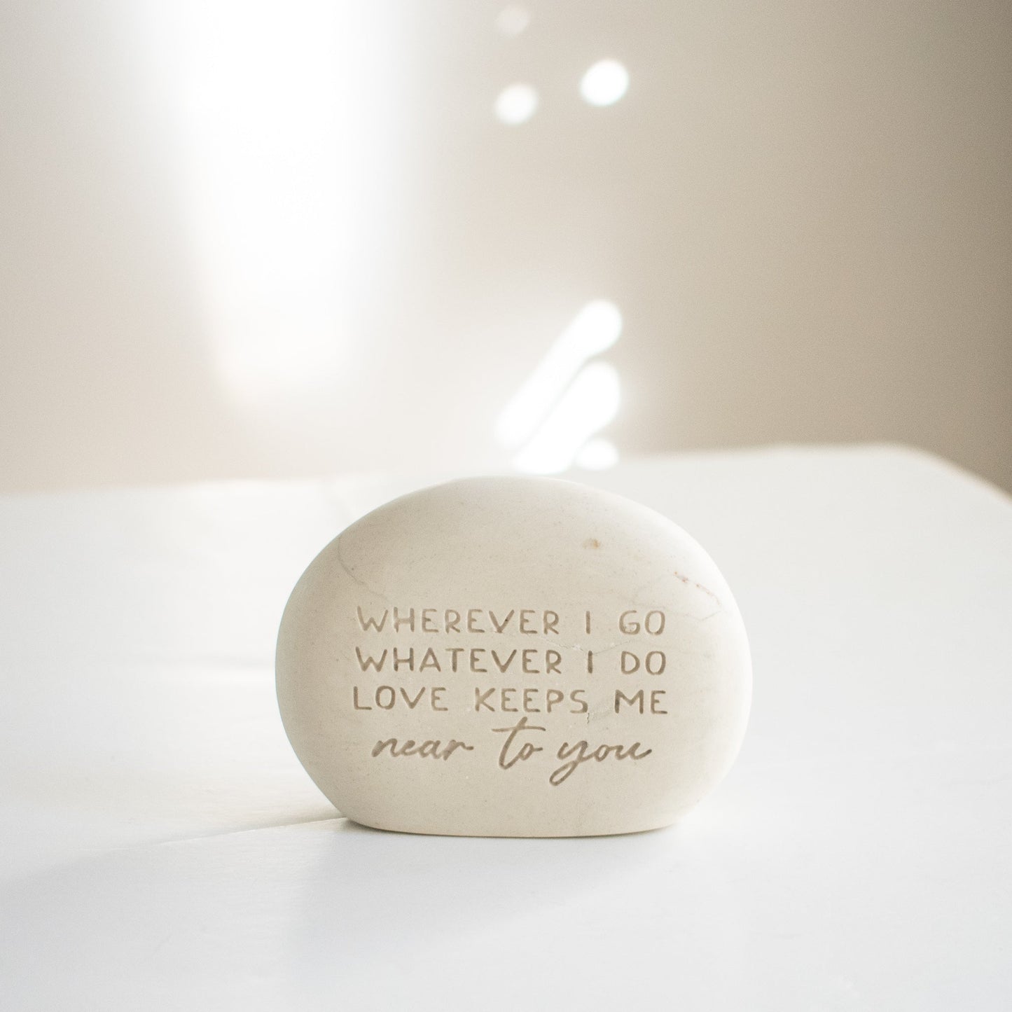 A memorial gemstone with Whenever I Go Whatever I Do Love Keeps Me Near To You engraved on it sitting on a white surface