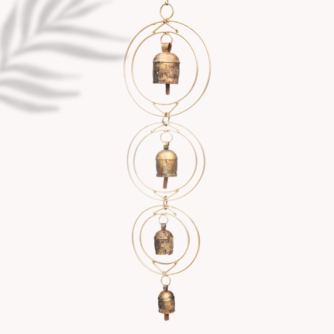 A rustic wind chime of recycled tin and iron coated in copper with four bells with a white background 
